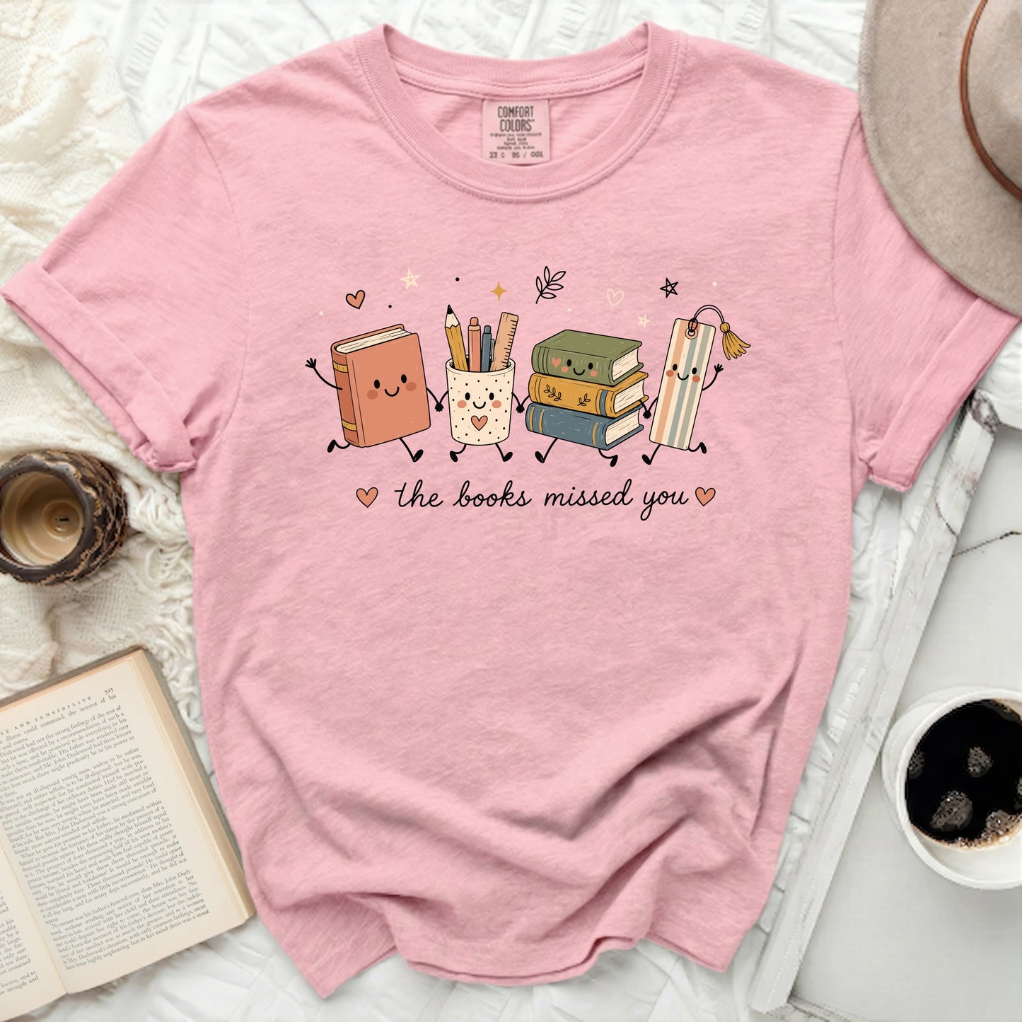 Pink t-shirt with graphic of books, pencil holder, and bookmark saying "the books missed you".