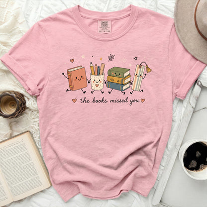 Pink t-shirt with graphic of books, pencil holder, and bookmark saying "the books missed you".