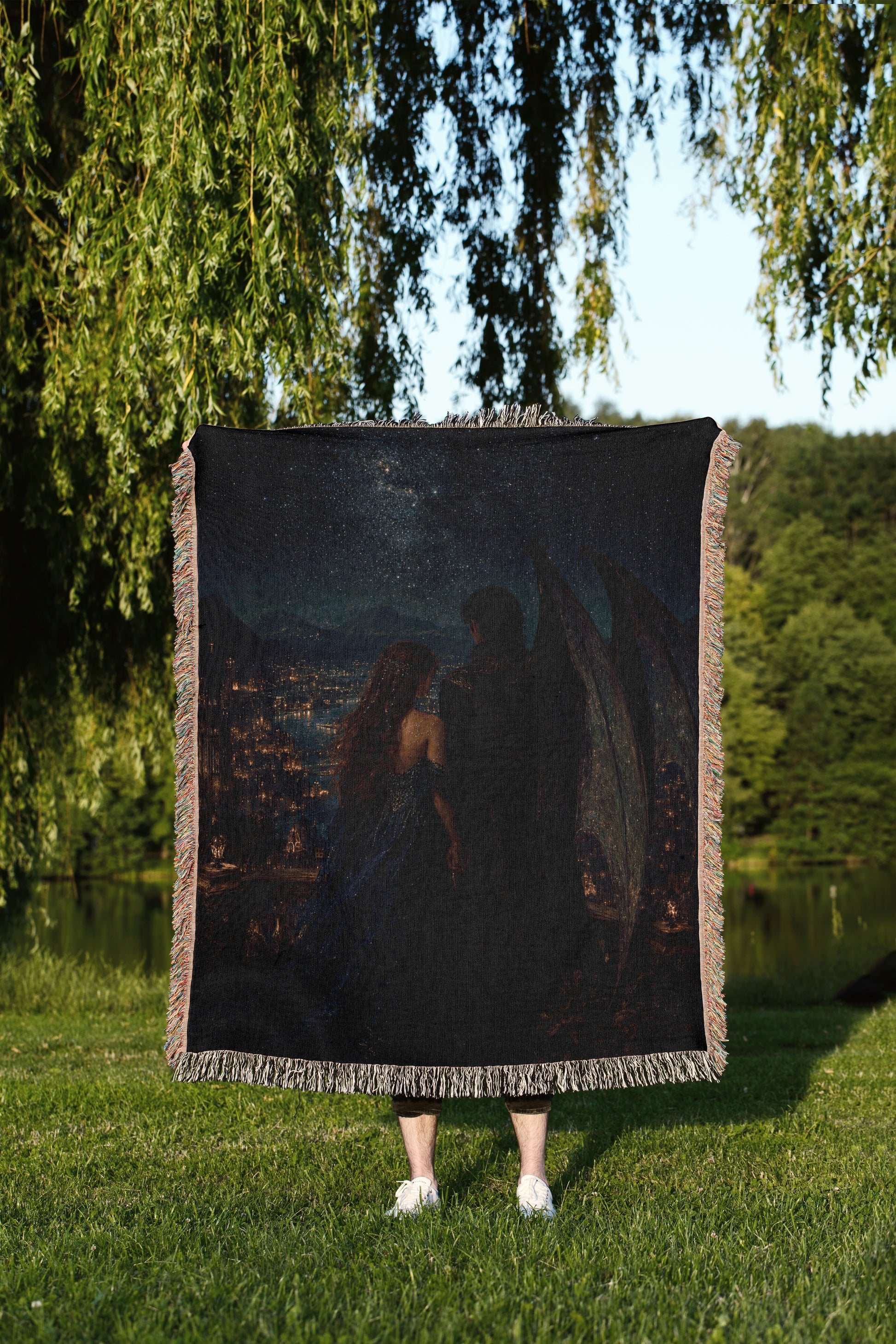 A person is standing in a grassy area, holding a large square blanket that features a painting of a couple.
