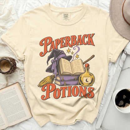 Cream t-shirt with "Paperback Potions" graphic of witch hat, books, and potion.