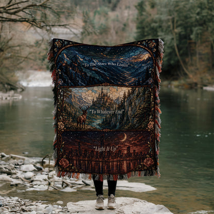 A person stands on a rock, holding a colorful blanket with a landscape scene and text printed on it, in front of a river and forest.