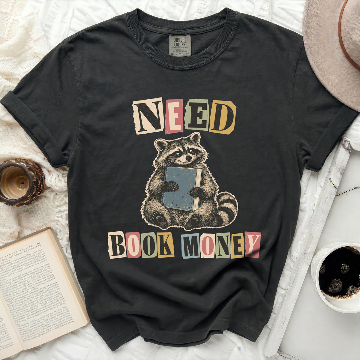 Black t-shirt with raccoon graphic and text "NEED BOOK MONEY".