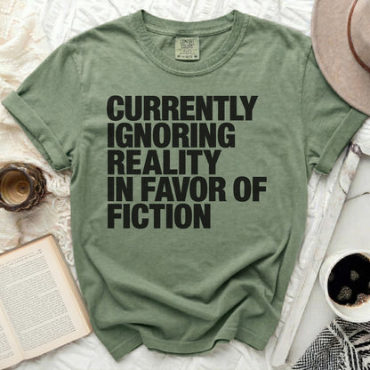 Olive green t-shirt with black text "Currently Ignoring Reality In Favor of Fiction".
