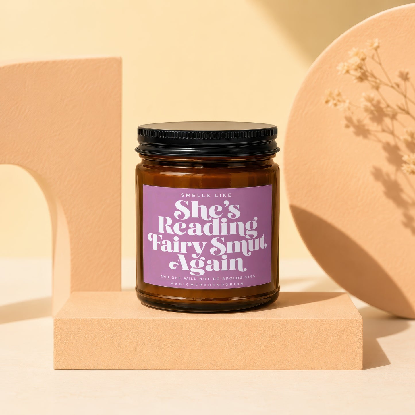 Amber candle with purple label reading "She's Reading Fairy Smut Again".