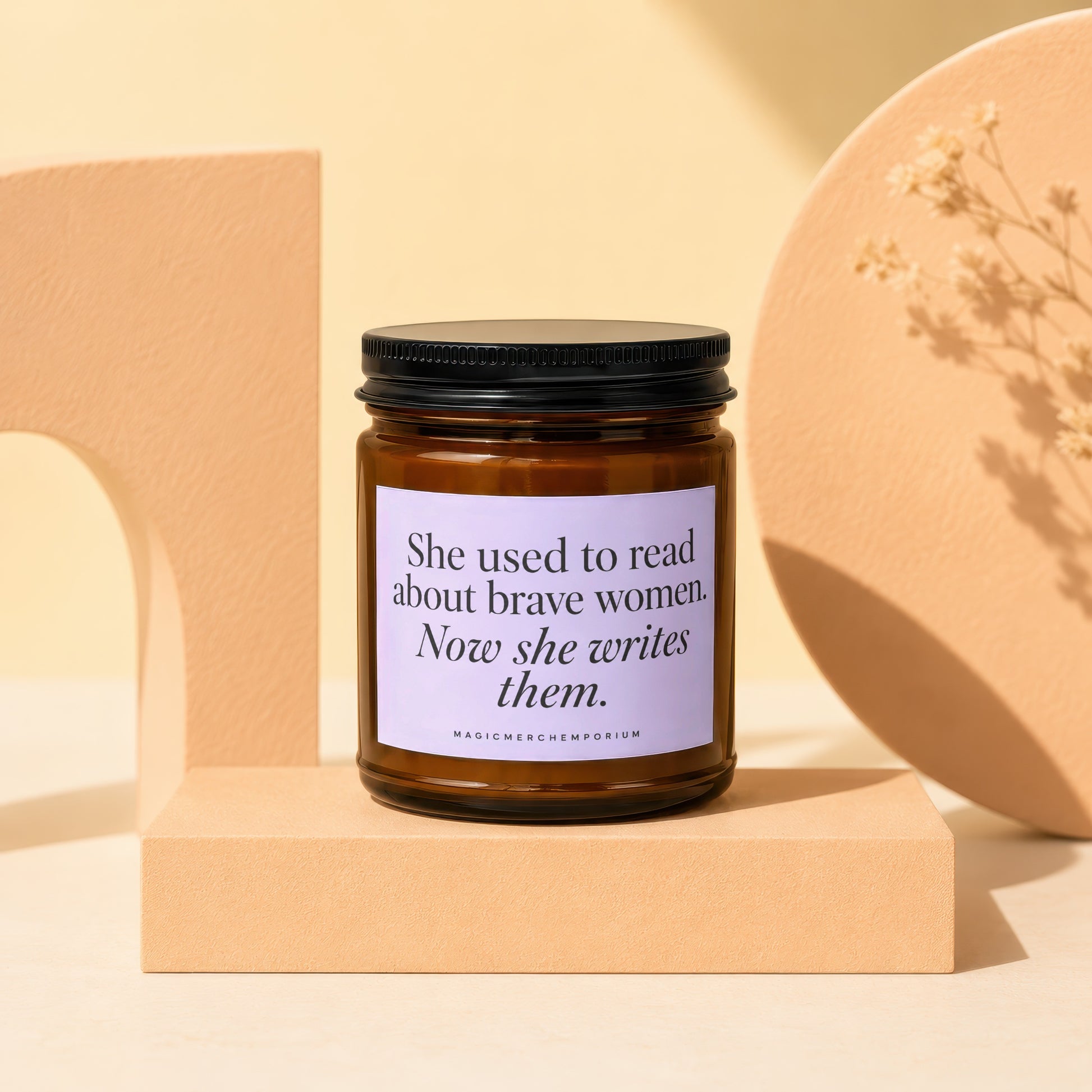 Amber jar candle with lavender label reading "She used to read about brave women. Now she writes them."