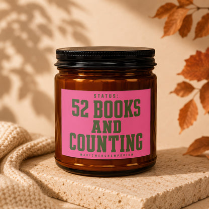 Amber candle with pink label reading "STATUS: 52 BOOKS AND COUNTING".