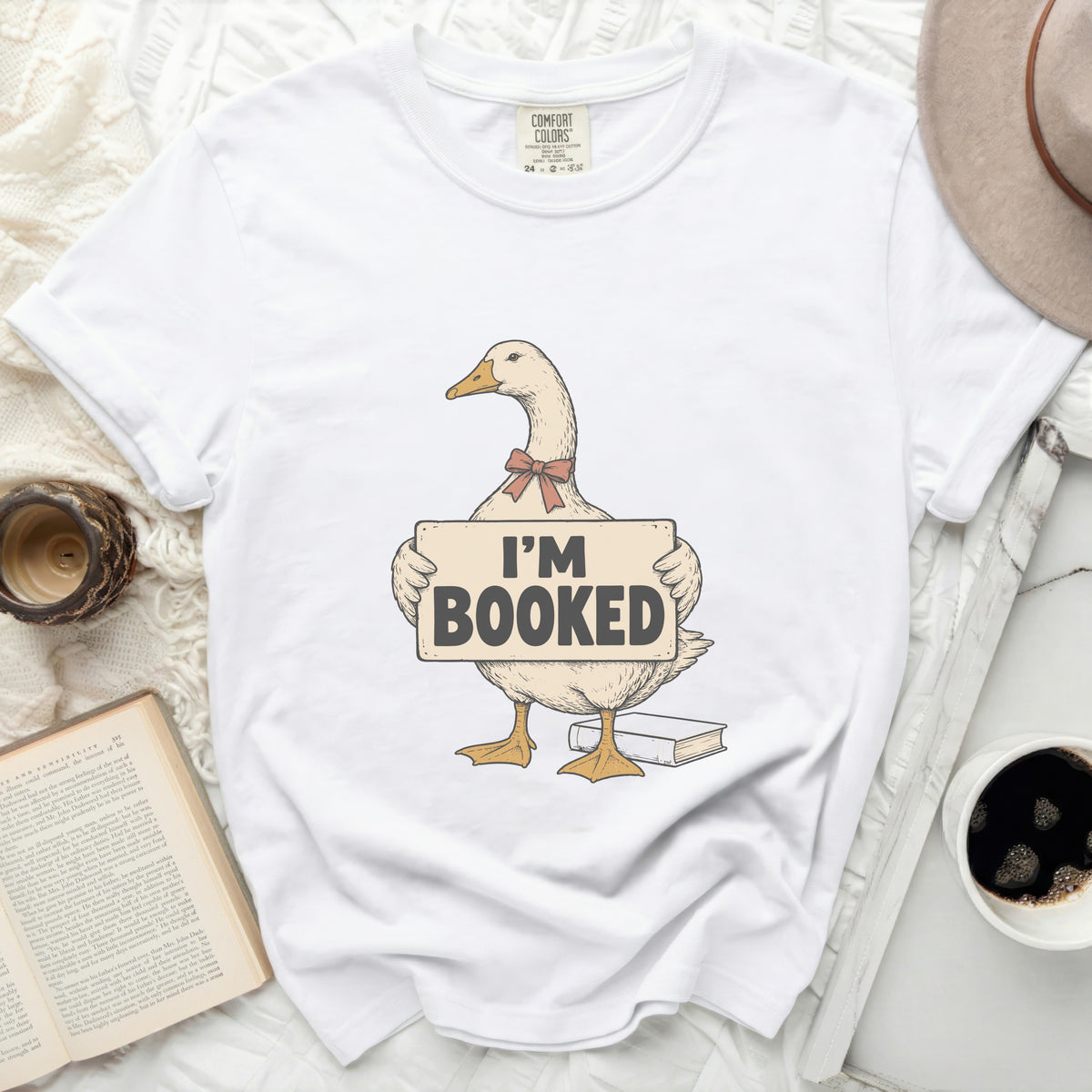White t-shirt with a goose graphic holding an "I'M BOOKED" sign.
