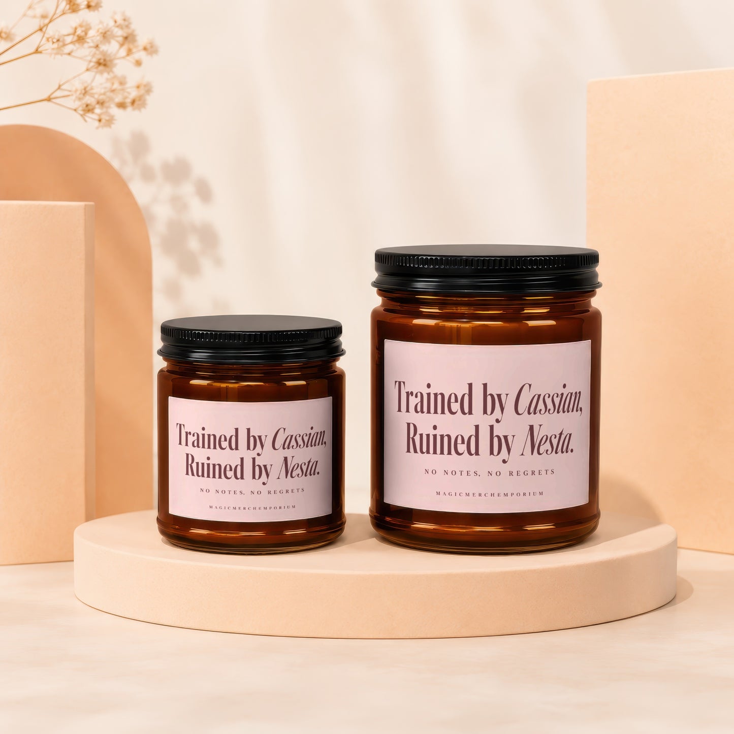 Two amber glass candles with black lids, labeled "Trained by Cassian, Ruined by Nesta."