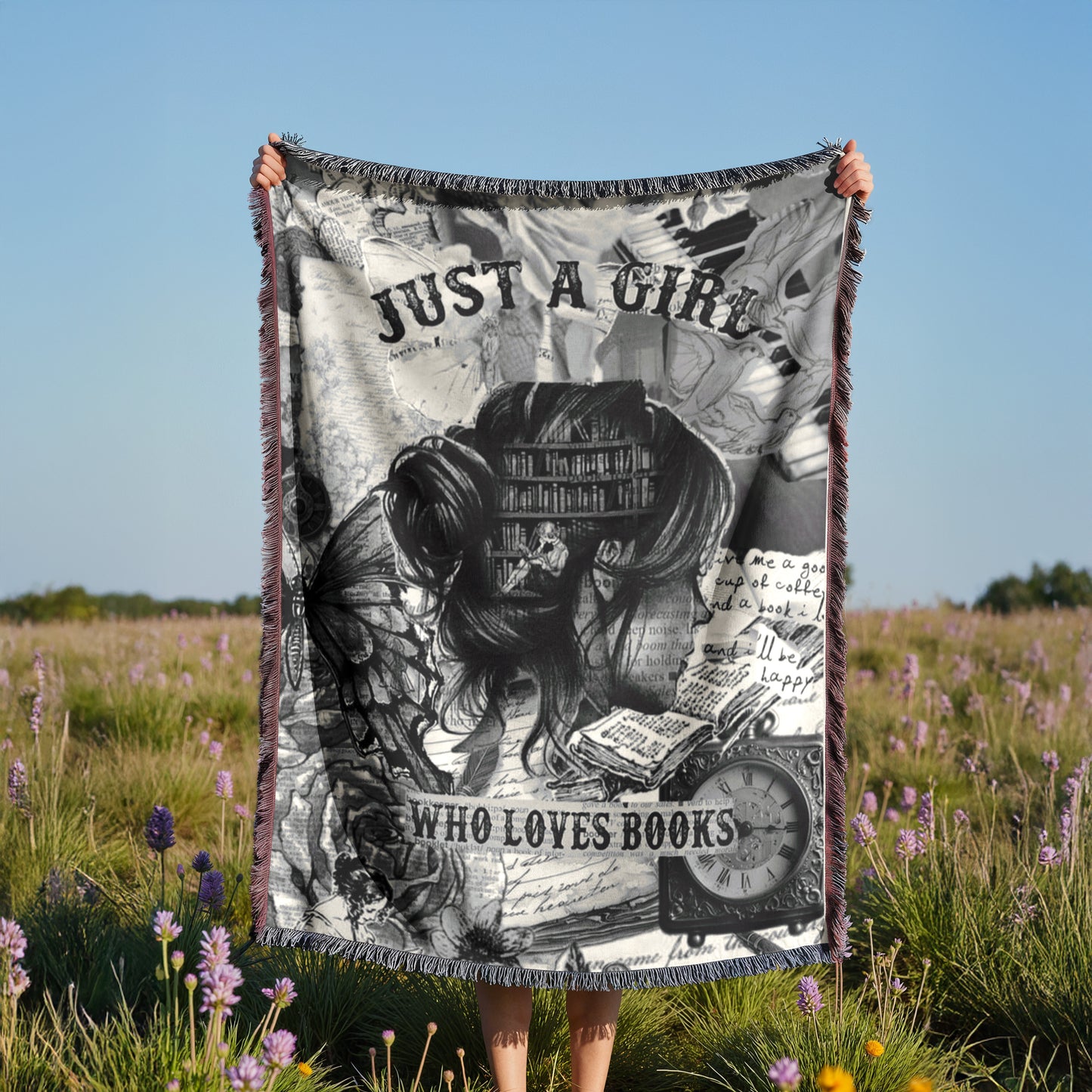 A person is holding up a blanket with a black and white image of a book and the text "Just a girl who loves books" against a field of purple flowers.
