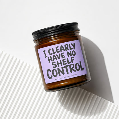 Amber candle jar with black lid featuring lavender label with text "I CLEARLY HAVE NO SHELF CONTROL".