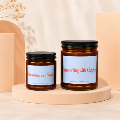 Two amber glass candles with black lids labeled "Introverting with Chapters".