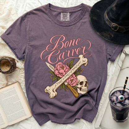 Purple t-shirt with "Bone Carver" text, skull, bones, knife, and flowers graphic.