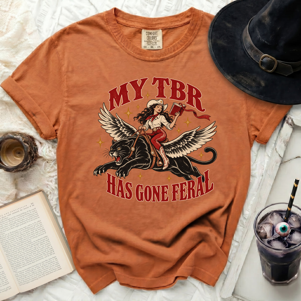 Orange t-shirt with graphic of woman riding winged panther, text "MY TBR HAS GONE FERAL".