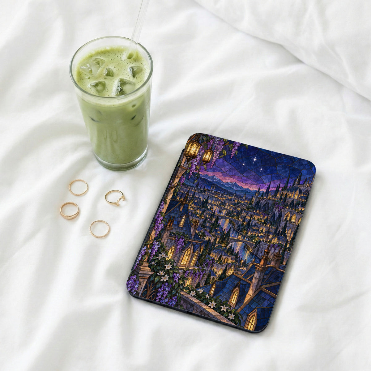 Tablet cover with stained-glass castle scene next to a matcha drink and rings.