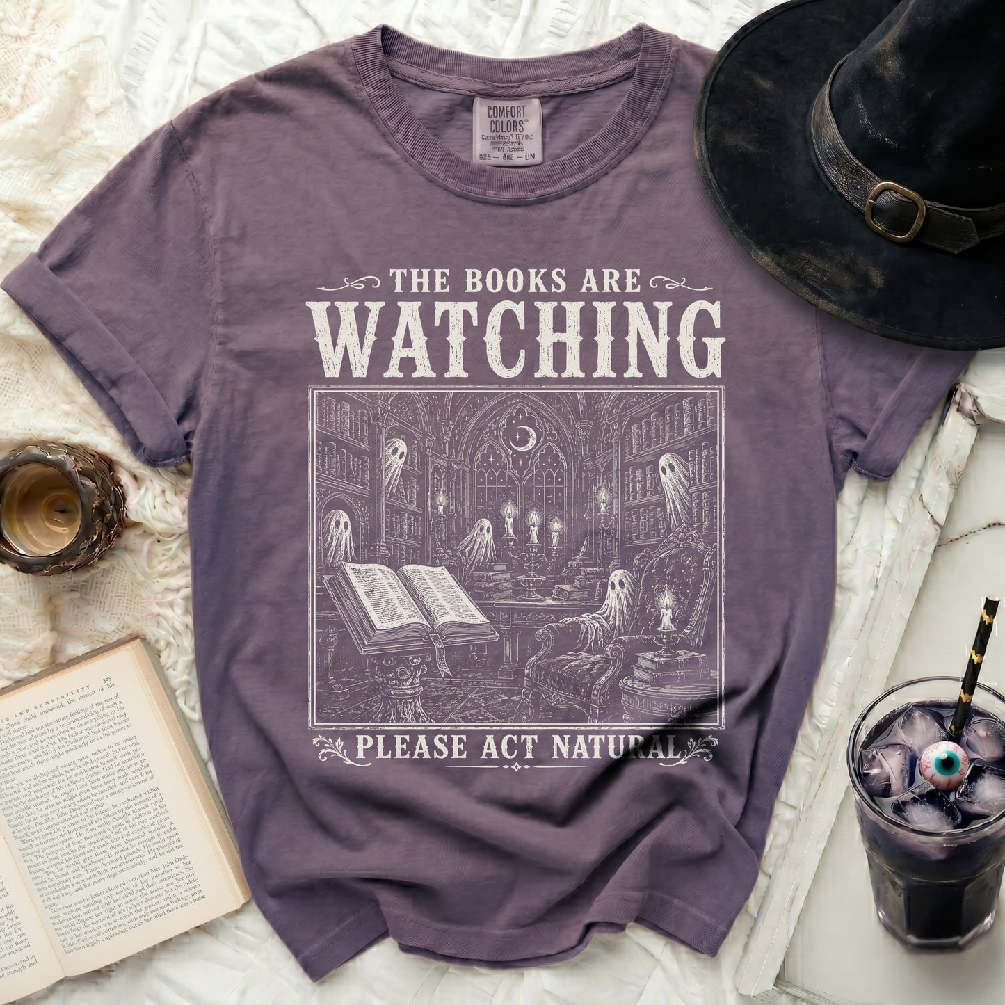 Purple t-shirt with "The Books Are Watching" and ghost library design.