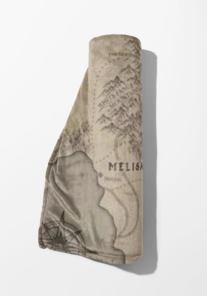 Rolled taupe blanket with a faded map pattern and the name "MELISA".