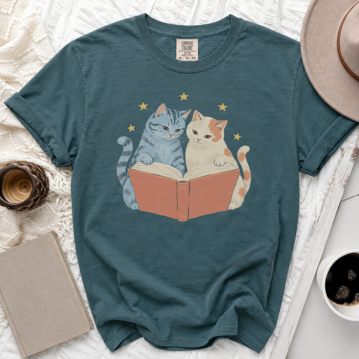 Teal t-shirt with graphic of two cats reading a book and yellow stars.