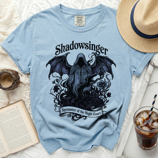 Light blue t-shirt with a dark graphic of a hooded figure with wings and text.