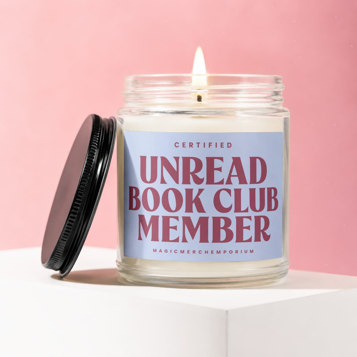 Glass candle with a lit wick, featuring a "Certified Unread Book Club Member" label.
