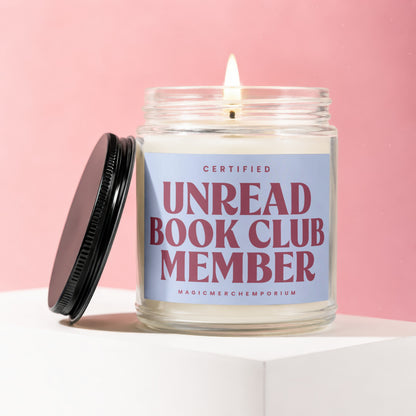 Glass candle with a lit wick, featuring a "Certified Unread Book Club Member" label.