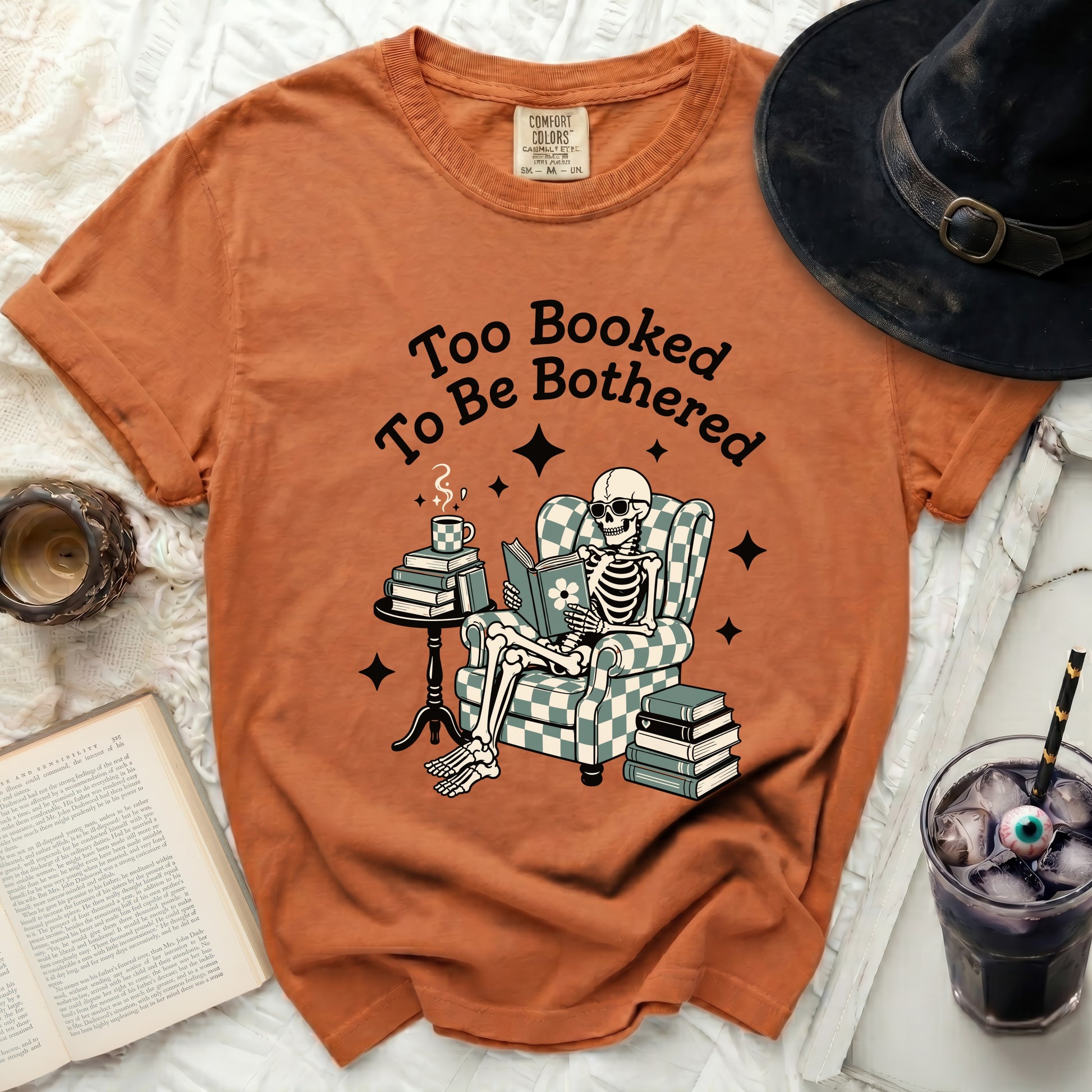 Orange t-shirt with a skeleton reading a book and text "Too Booked To Be Bothered."