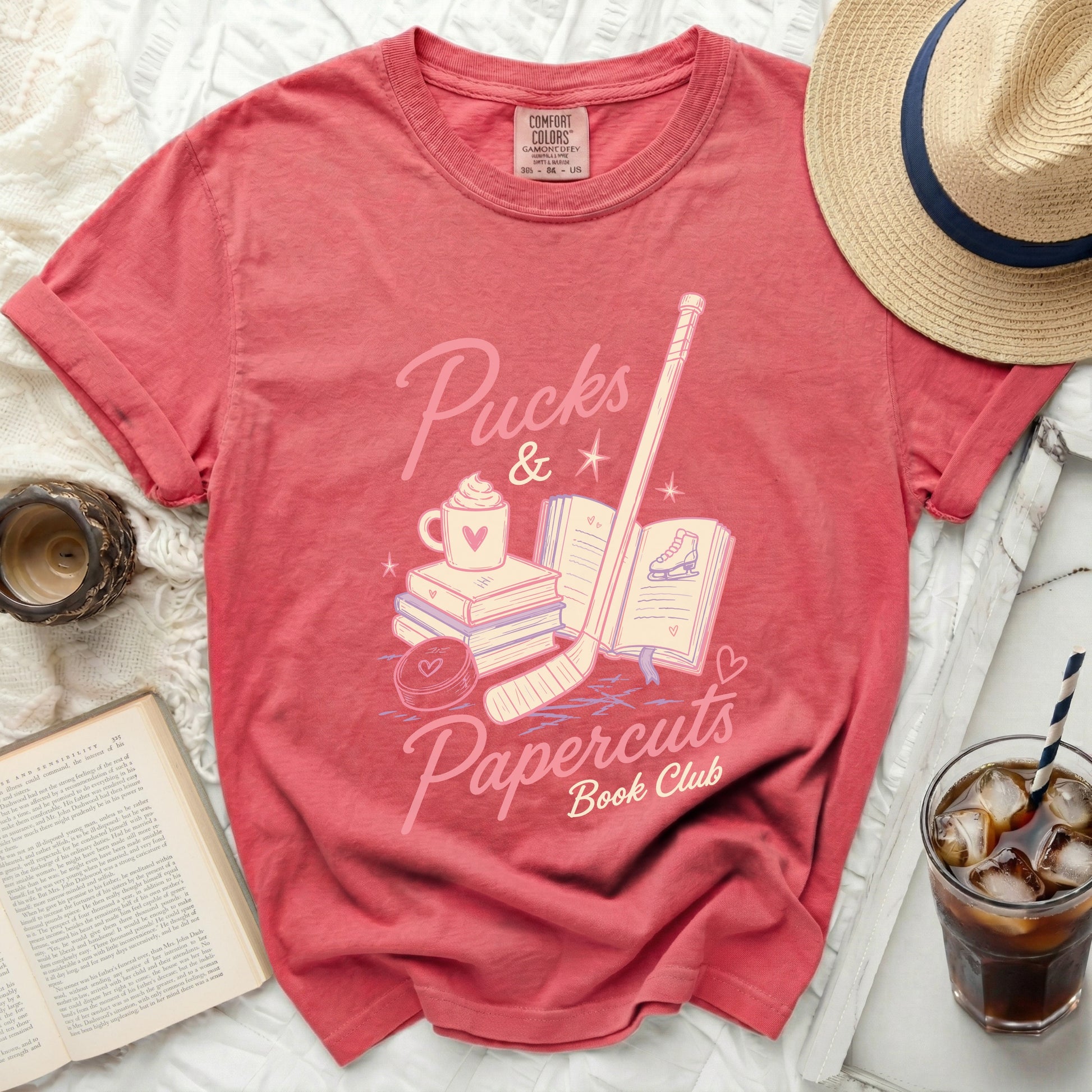 Coral t-shirt with "Pucks & Papercuts Book Club" graphic.