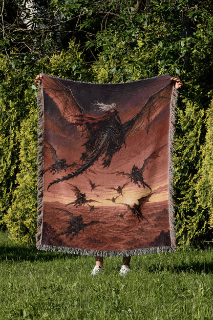 A person is holding up a large tapestry or blanket with a dragon design on it, standing in a grassy area with trees in the background.