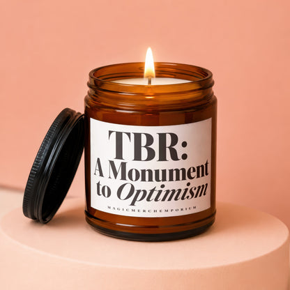 Lit amber glass candle with "TBR: A Monument to Optimism" text.