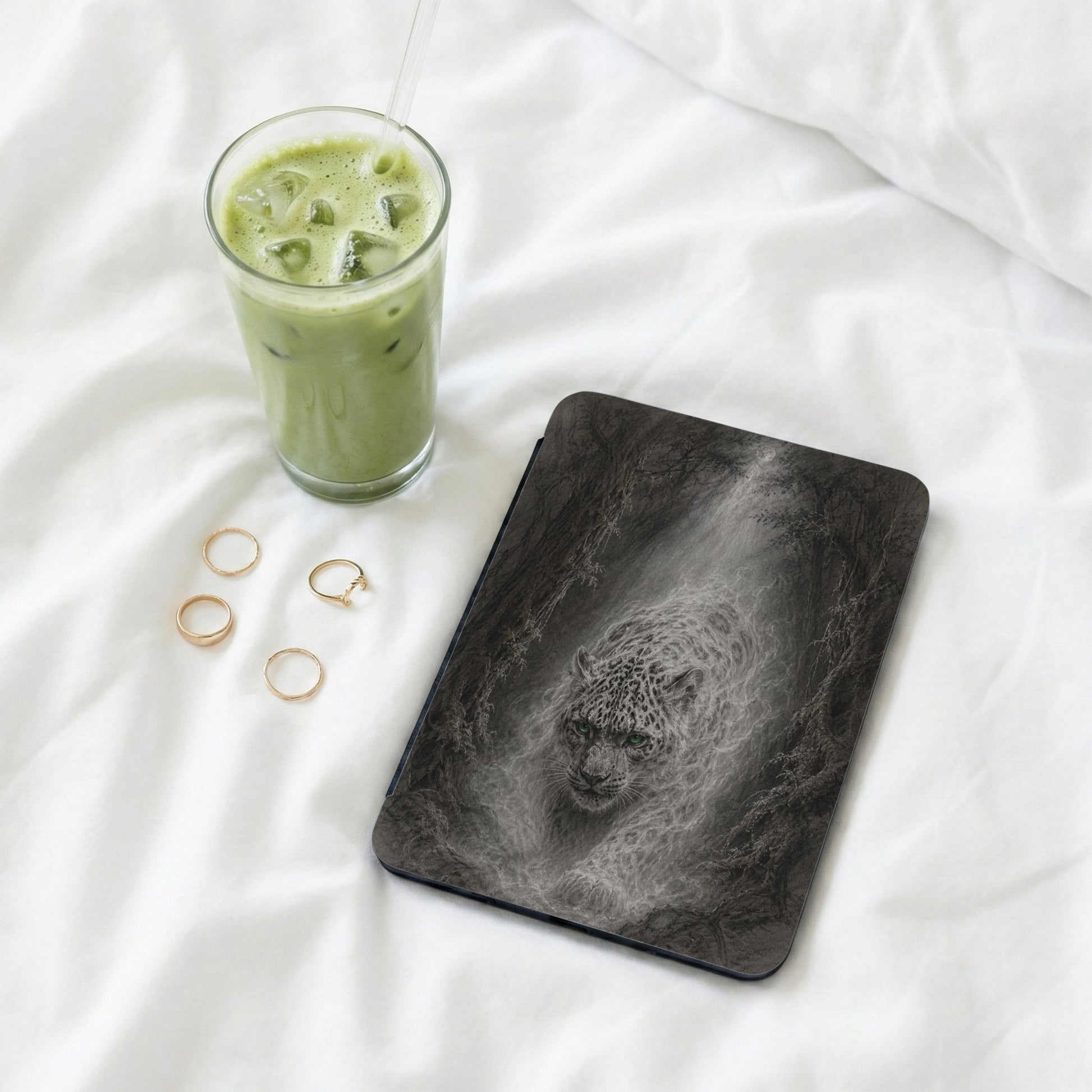 Luminous leopard emerging from dark forest on a case, with matcha drink and rings.