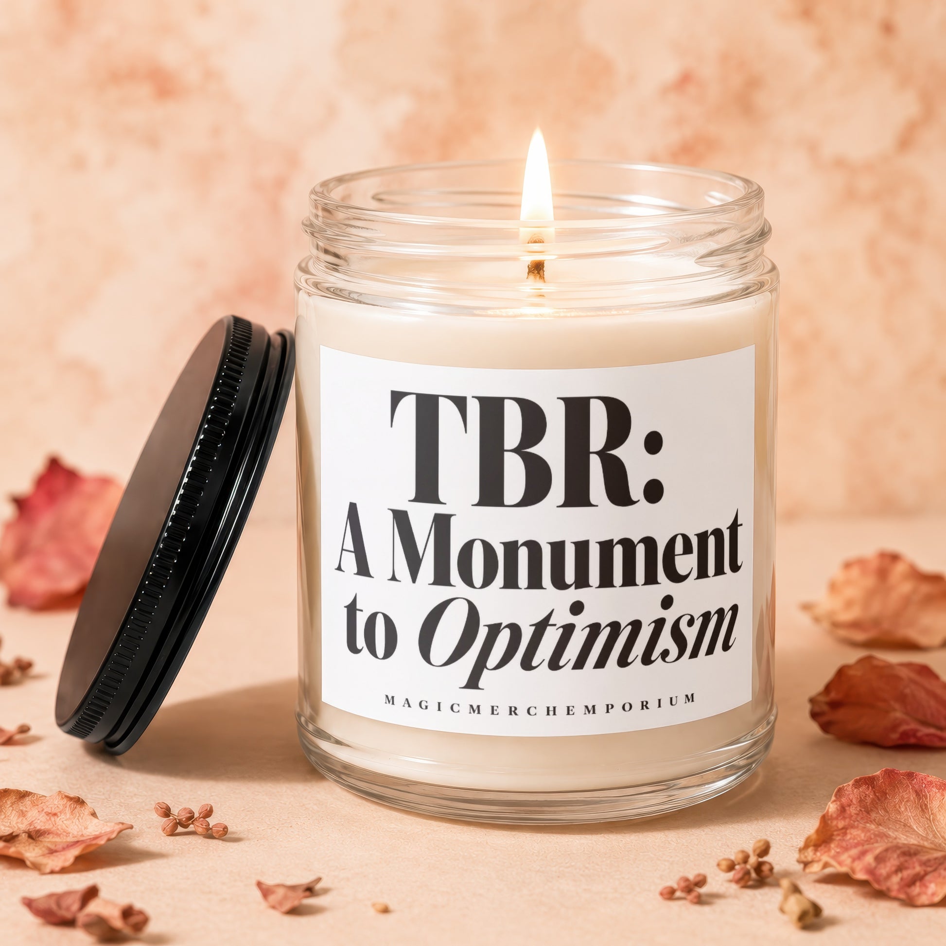 Candle with lid off, displaying text "TBR: A Monument to Optimism" and brand.