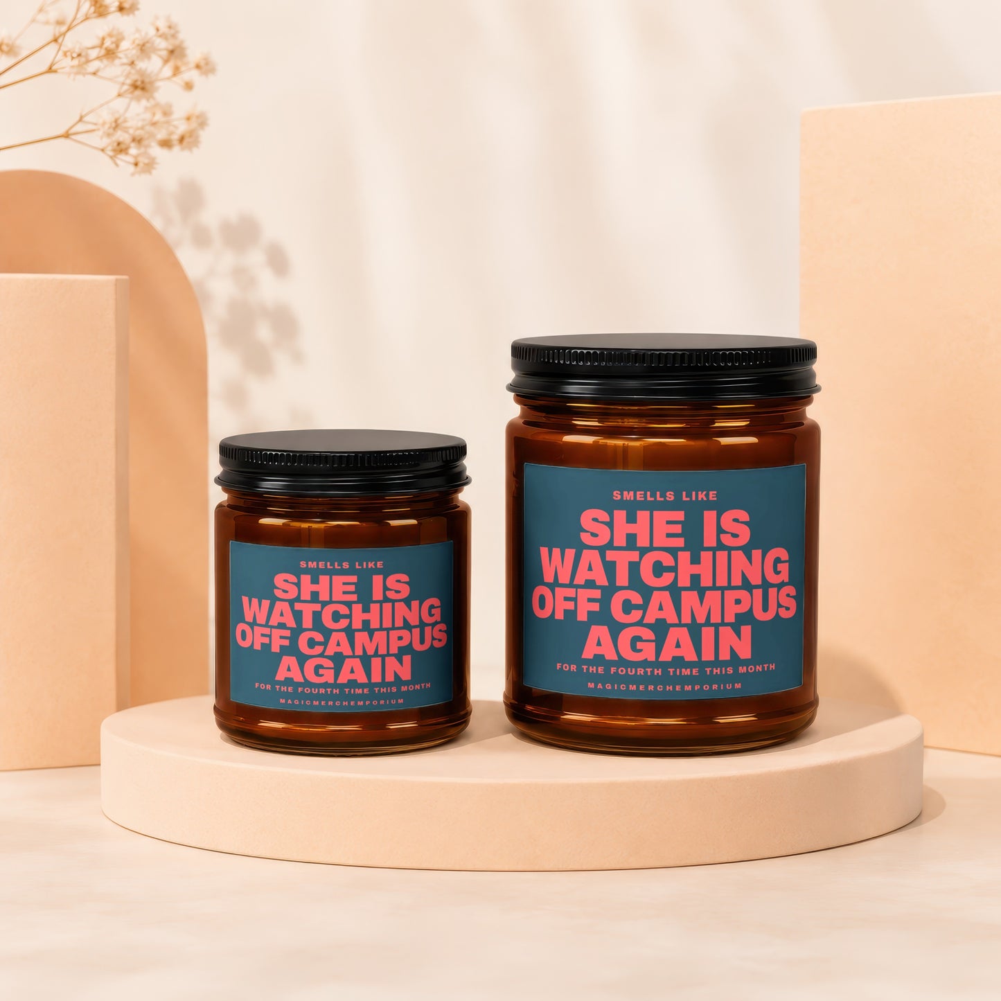 Two amber glass candles with black lids, one larger than the other, featuring teal labels with pink text.