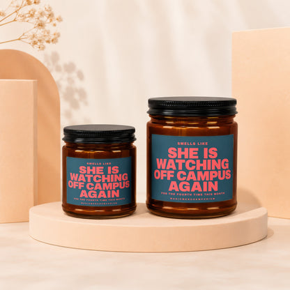 Two amber glass candles with black lids, one larger than the other, featuring teal labels with pink text.