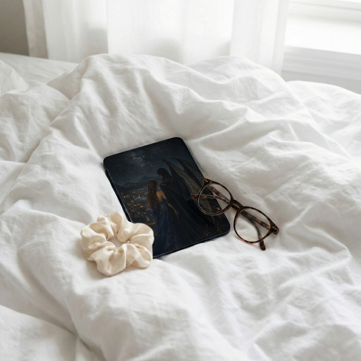 Book with fantasy cover, glasses, and scrunchie on rumpled white sheets.