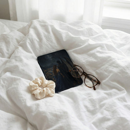 Book with fantasy cover, glasses, and scrunchie on rumpled white sheets.