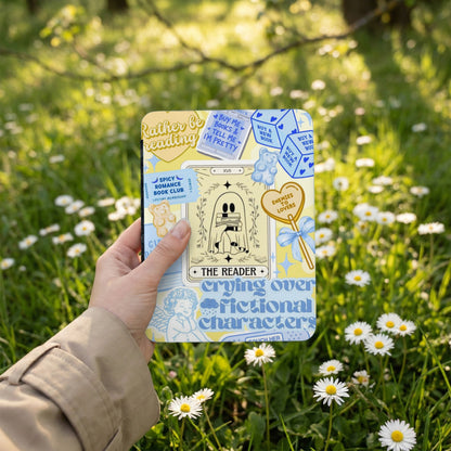 "The Reader" tarot card design with text on a square object held outdoors.