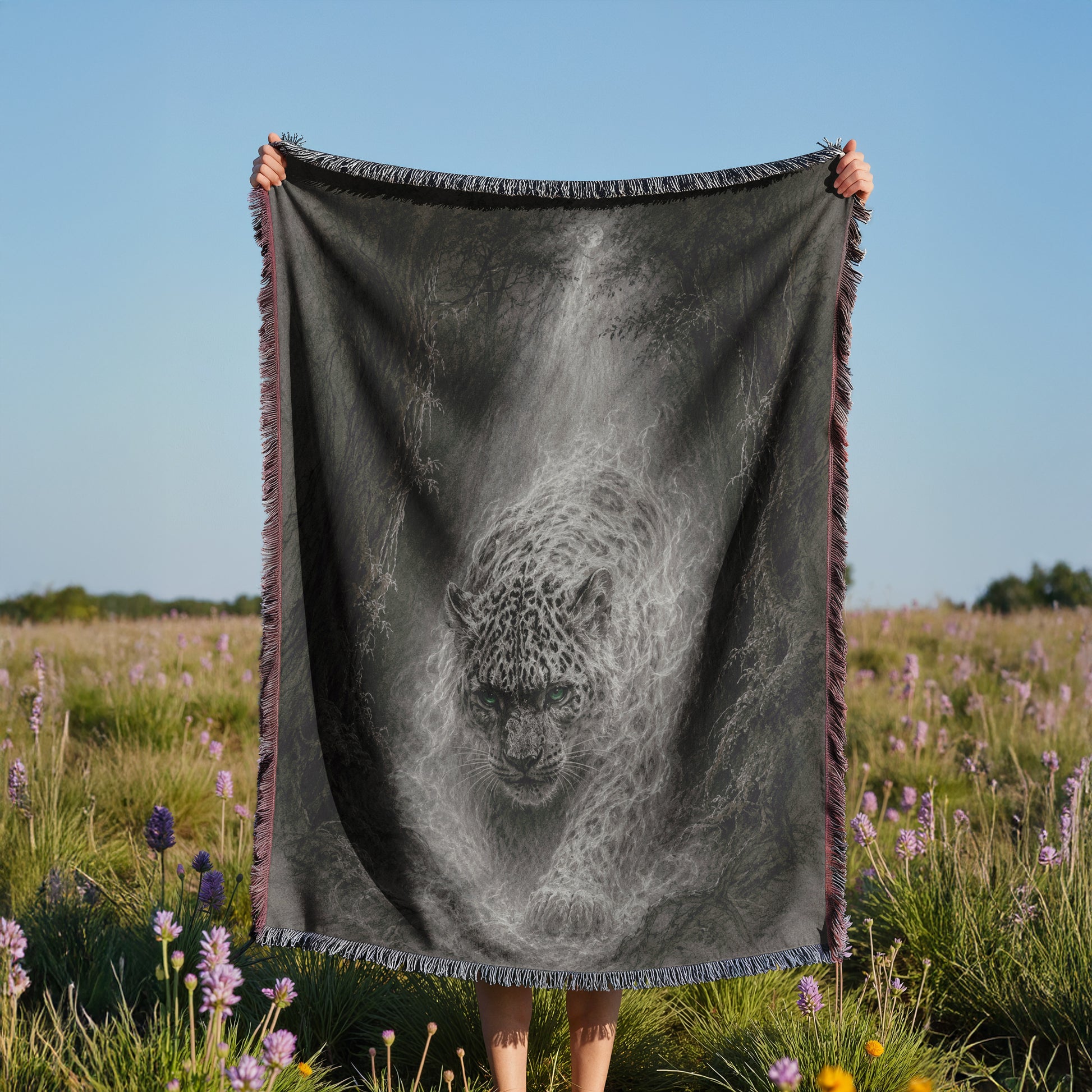 A person is holding a large black and white blanket with a leopard image on it, standing in a field with purple flowers.