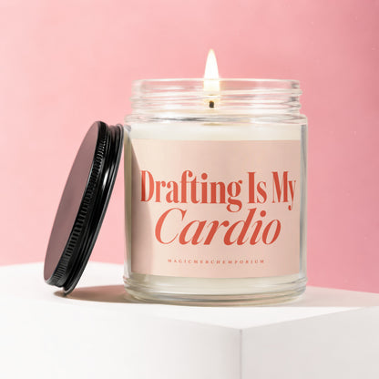 Lit jar candle with pink label reading "Drafting Is My Cardio" on pink background.