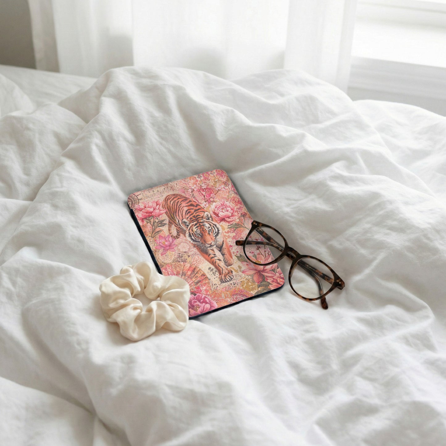 Tiger and floral patterned book with glasses and scrunchie on white sheets.