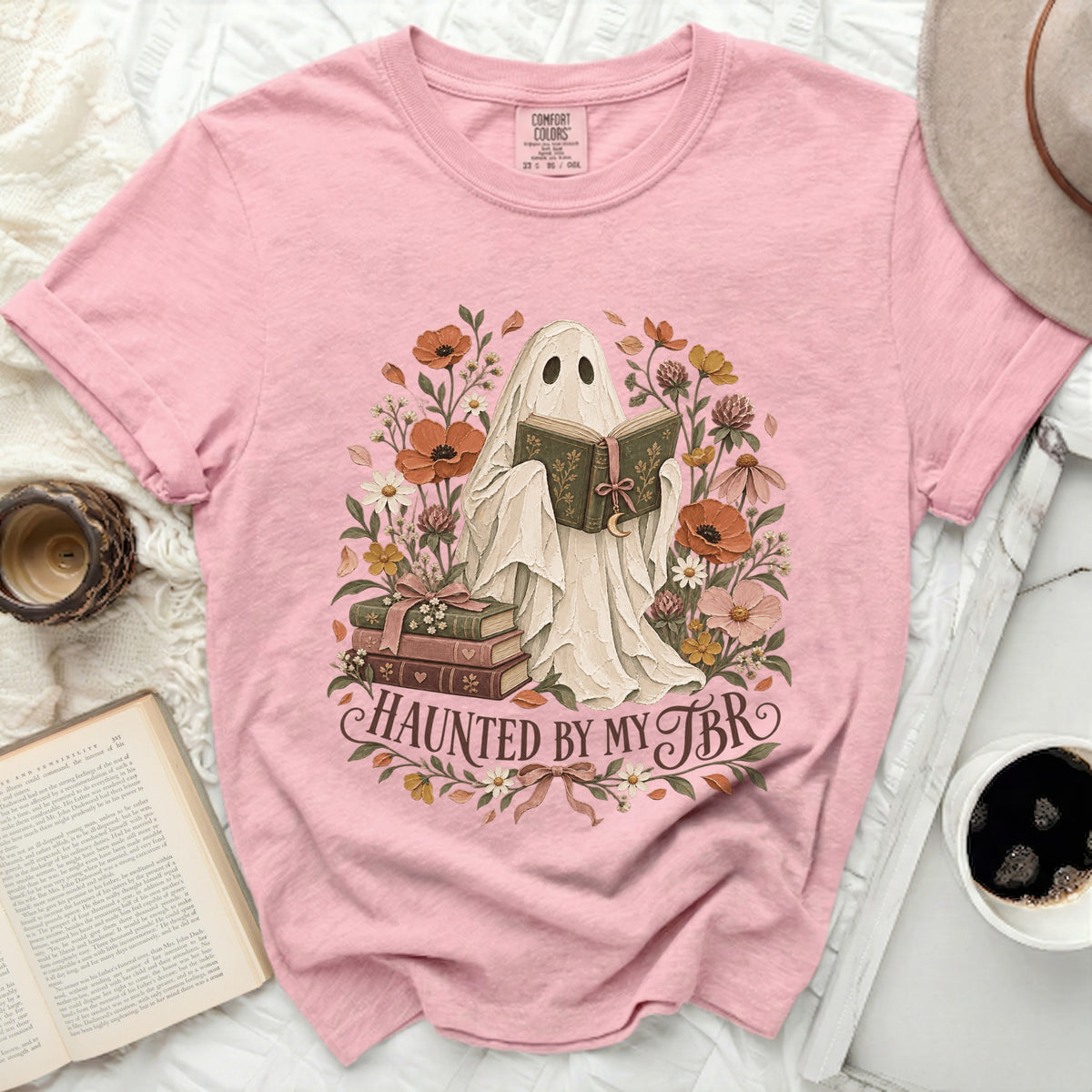 Pink t-shirt with a ghost reading a book and the text "HAUNTED BY MY TBR".