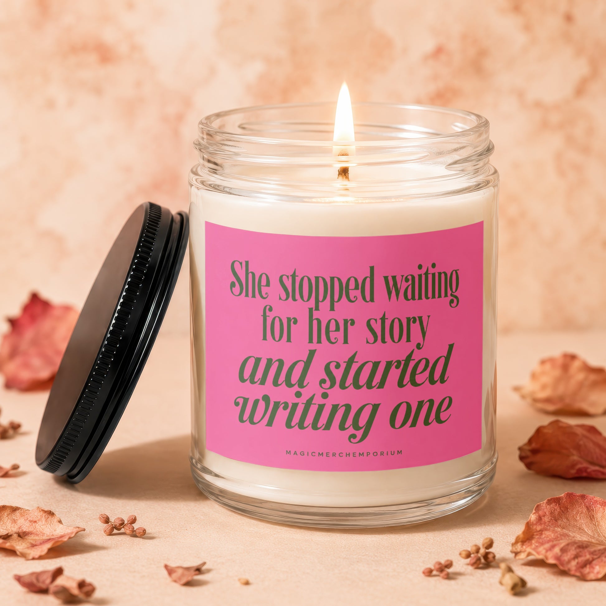 Glass candle with pink label reading "She stopped waiting for her story and started writing one."