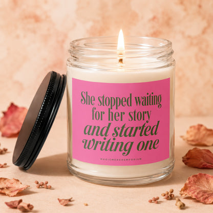 Glass candle with pink label reading "She stopped waiting for her story and started writing one."