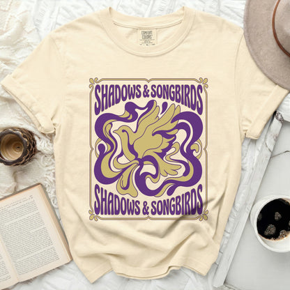 Cream t-shirt with "Shadows & Songbirds" graphic featuring a stylized bird.