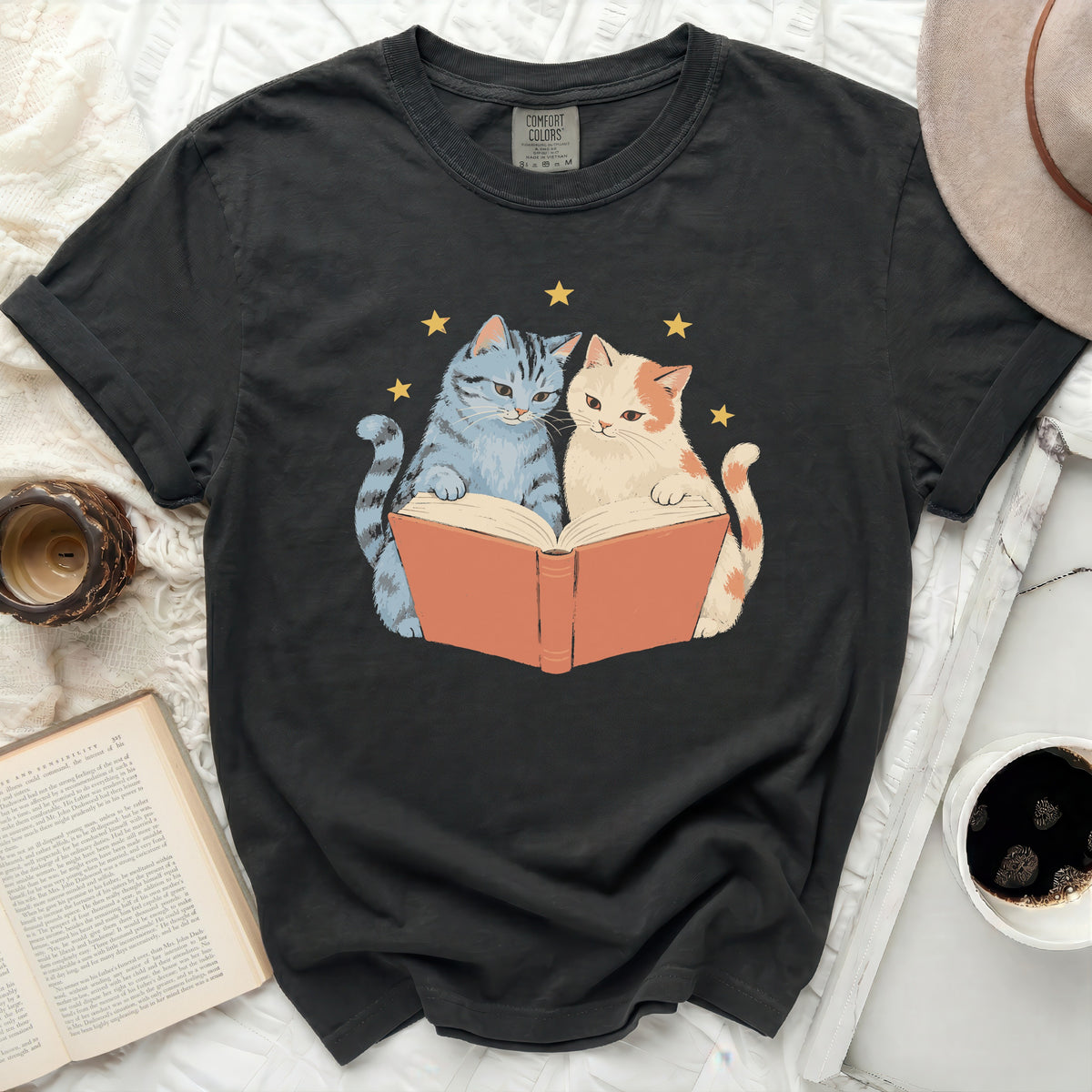 T-shirt with a graphic of two cats reading a book under stars.