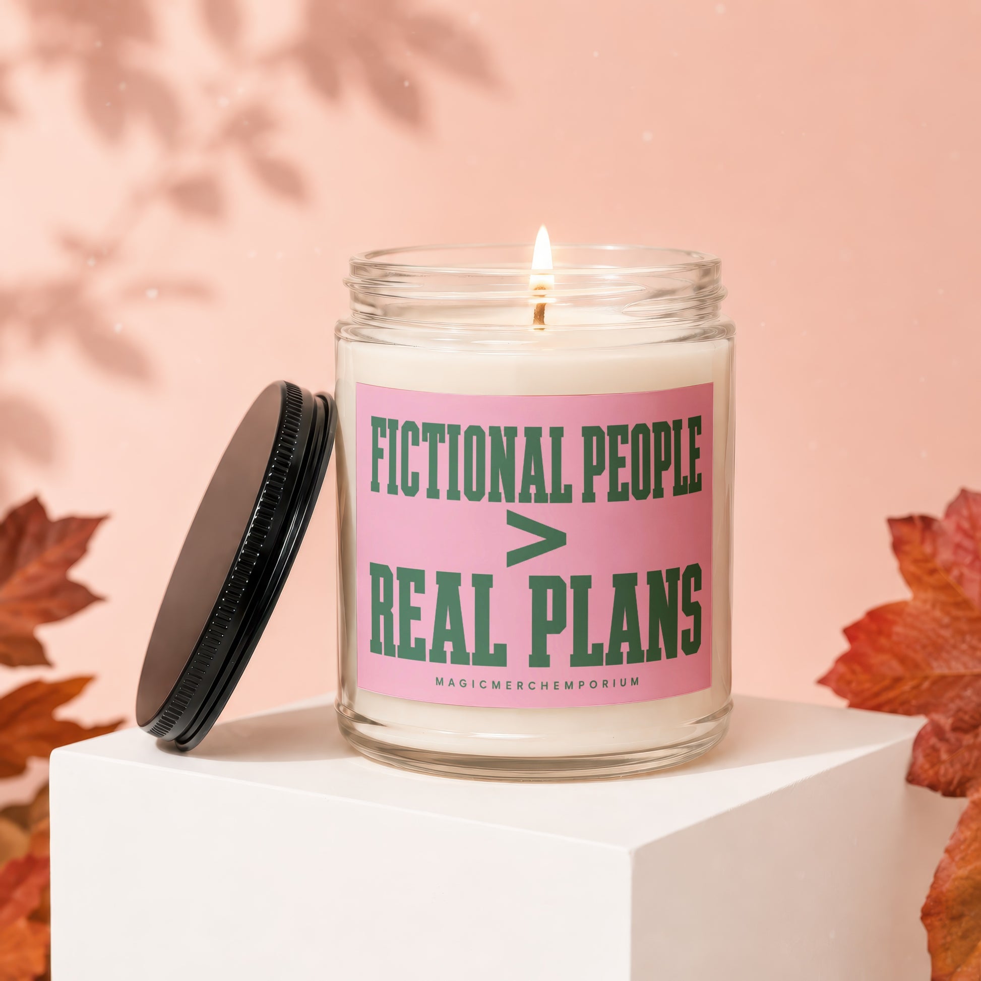 Glass candle with "FICTIONAL PEOPLE > REAL PLANS" text on pink label.