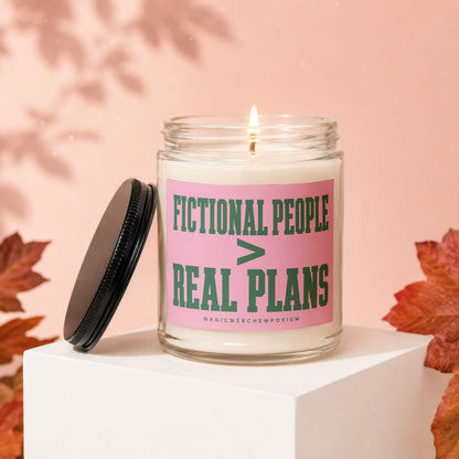 Glass candle with "FICTIONAL PEOPLE > REAL PLANS" text on pink label.