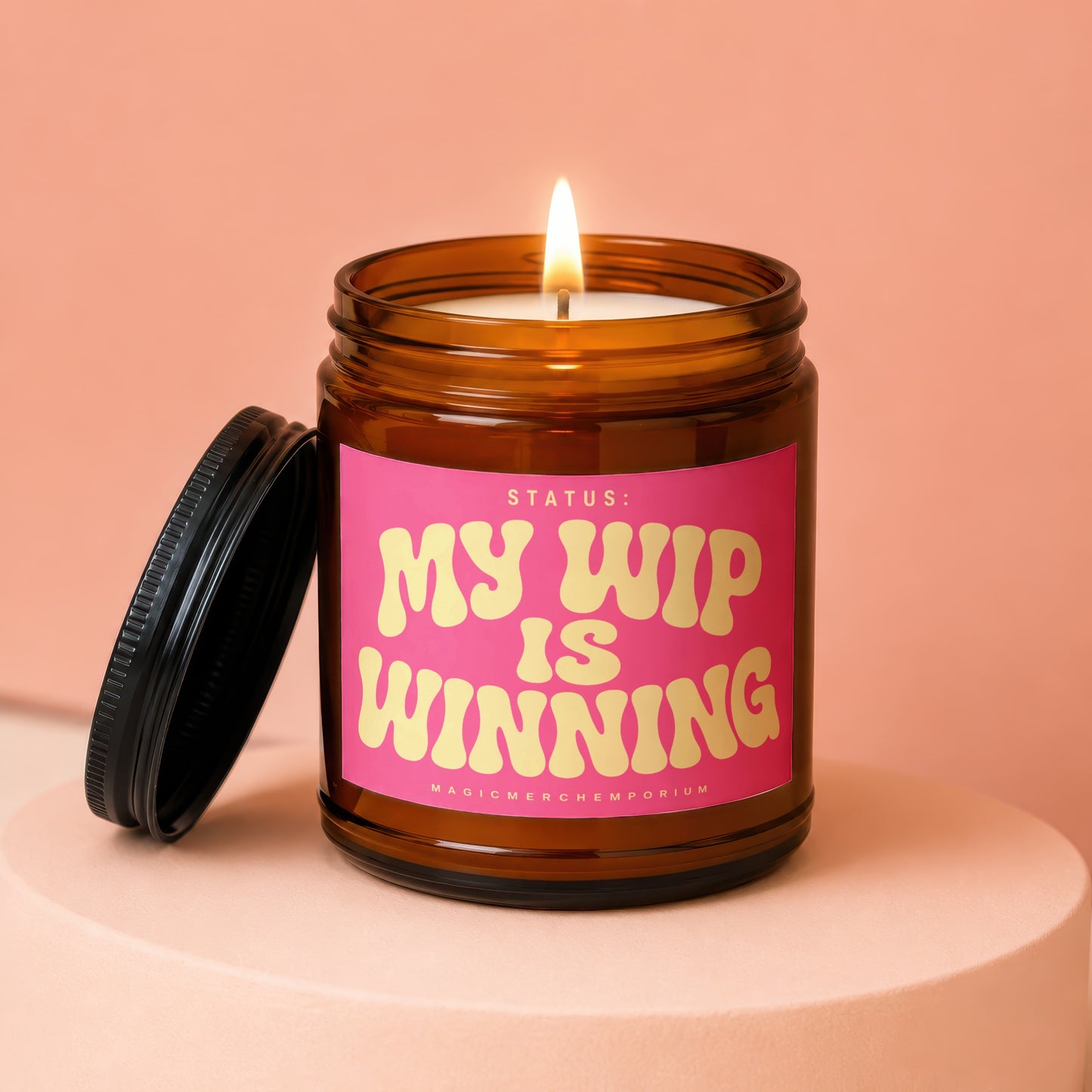 Amber jar candle with lit flame and pink label that reads "My WIP is Winning".