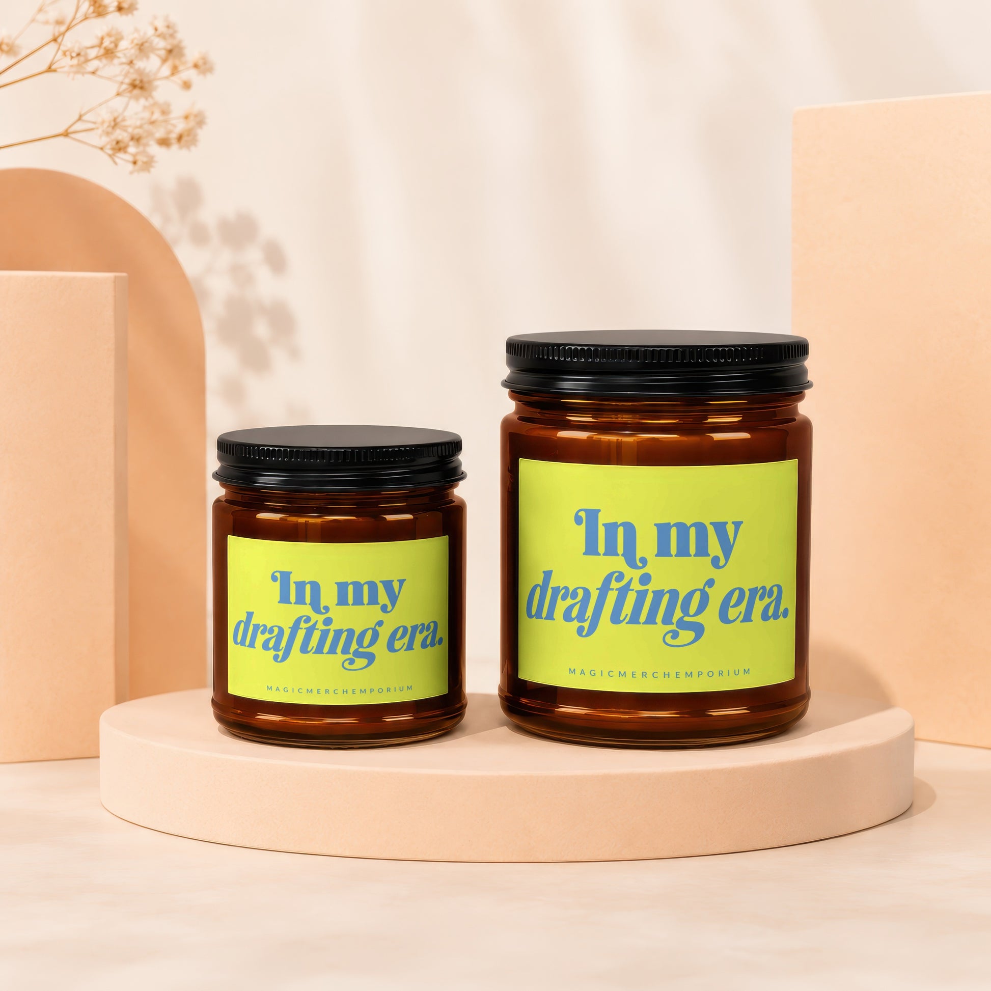 Two amber glass candles with black lids, featuring yellow labels with blue text.