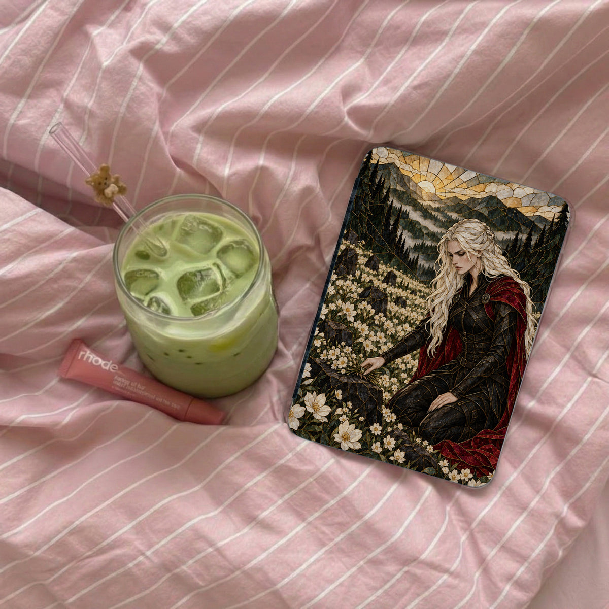 Phone case with fantasy art of woman in armor amidst flowers, next to matcha drink.