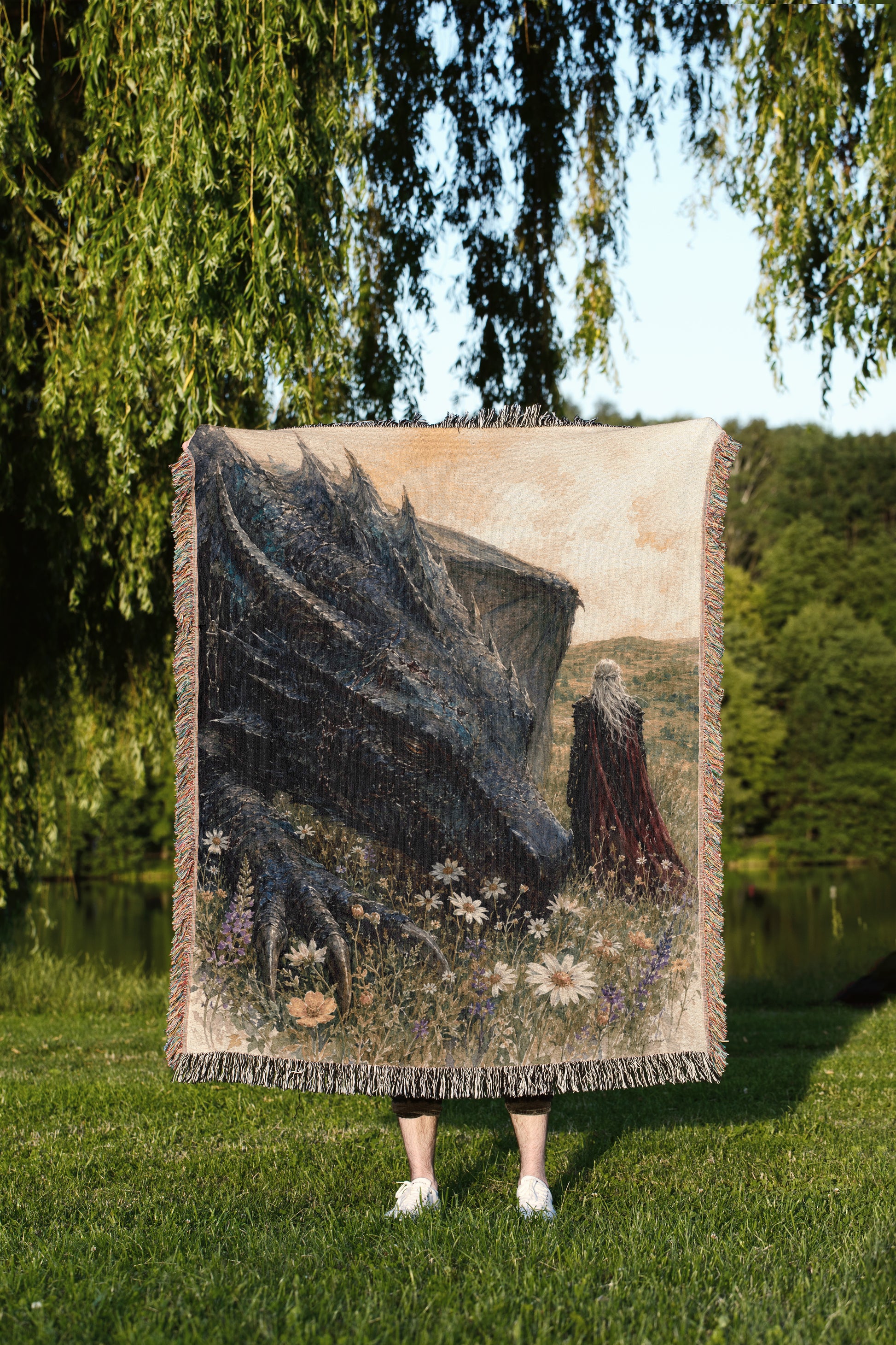 A person is standing in a grassy field, holding a large tapestry or blanket that features a dragon and a woman.