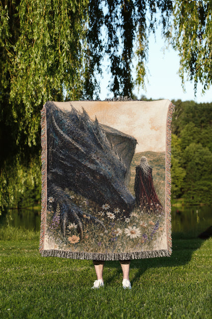 A person is standing in a grassy field, holding a large tapestry or blanket that features a dragon and a woman.